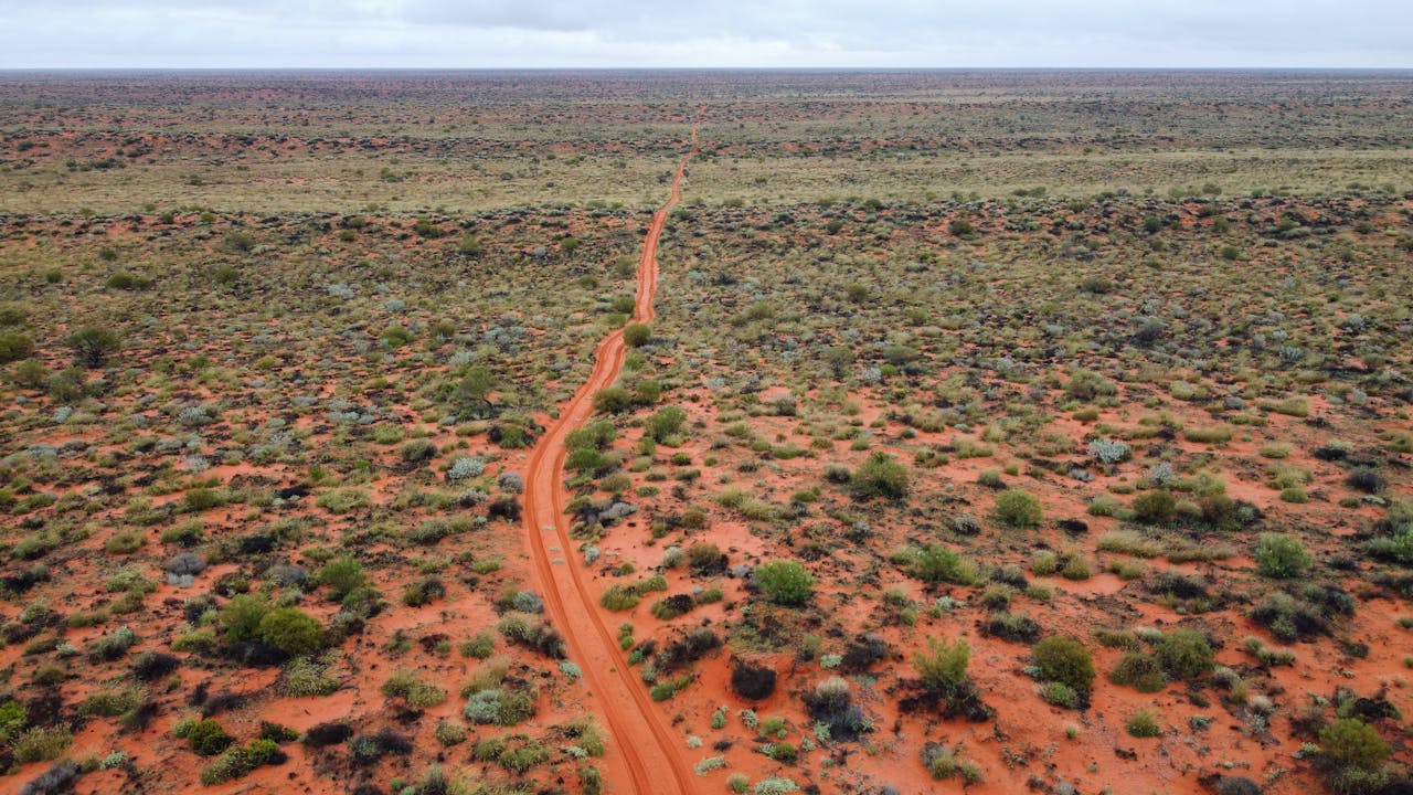services-03 Explore the vast and rugged Australian Outback with this stunning aerial view showcasing a remote dirt road stretching to the horizon.