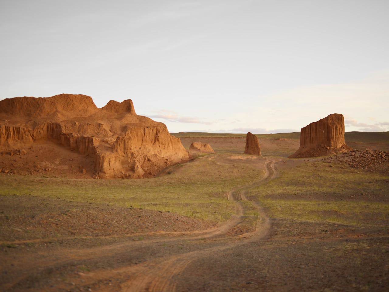 Explore the serene beauty of rugged red rock formations and open grasslands under a clear sky.